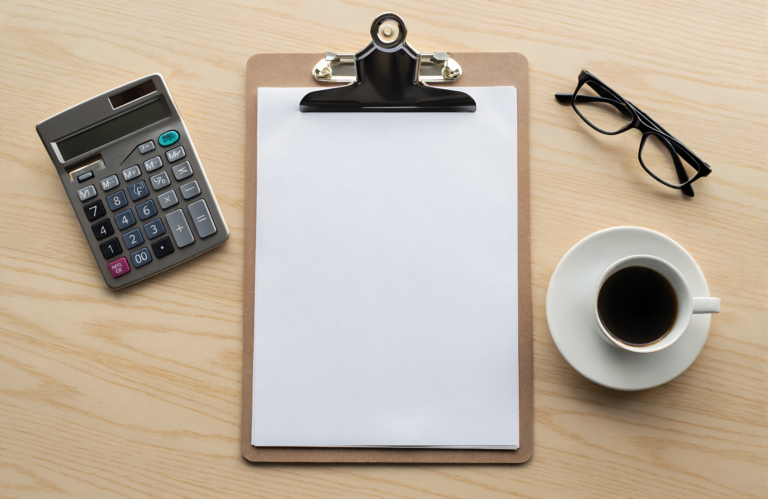 A clipboard, calculator and reading glasses on a desk