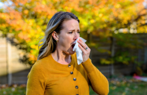 Woman sneezing into a tissue outdoors near ragweed in Covington, seasonal allergies