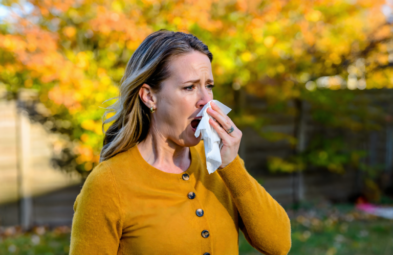 Woman sneezing into a tissue outdoors near ragweed in Covington, seasonal allergies
