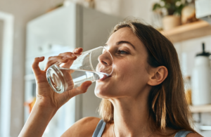 Woman in a sunny Covington kitchen drinking a tall glass of water to help flush a UTI