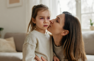 Mother comforting her young daughter who has red, irritated pink eye at home in Covington