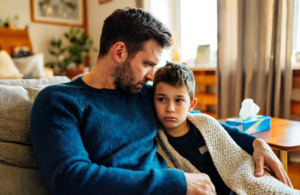 Father comforting his sick young son wrapped in a blanket at home near Mandeville, LA