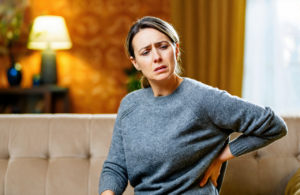 A woman at home holding her lower back with flank pain, a kidney infection symptom