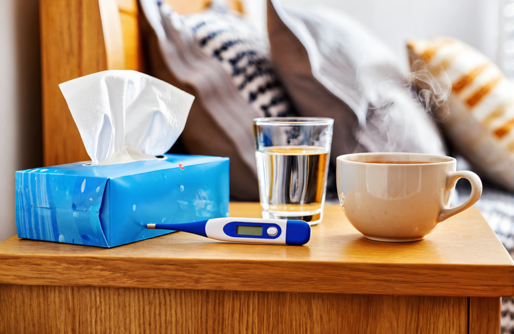Home nightstand with tissues, a thermometer, water and tea for adult RSV symptom care