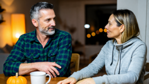 A couple at their dining table on a fall evening, talking over plans for an annual physical in Covington, LA, a pumpkin and mug beside them